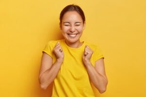 si-finalmente-exito-alegre-chica-coreana-aprieta-punos-triunfo-cierra-ojos-felicidad-alegria-tiene-sonrisa-dientes-viste-atuendo-informal-aislado-pared-amarilla-triunfa-victoria_273609-2